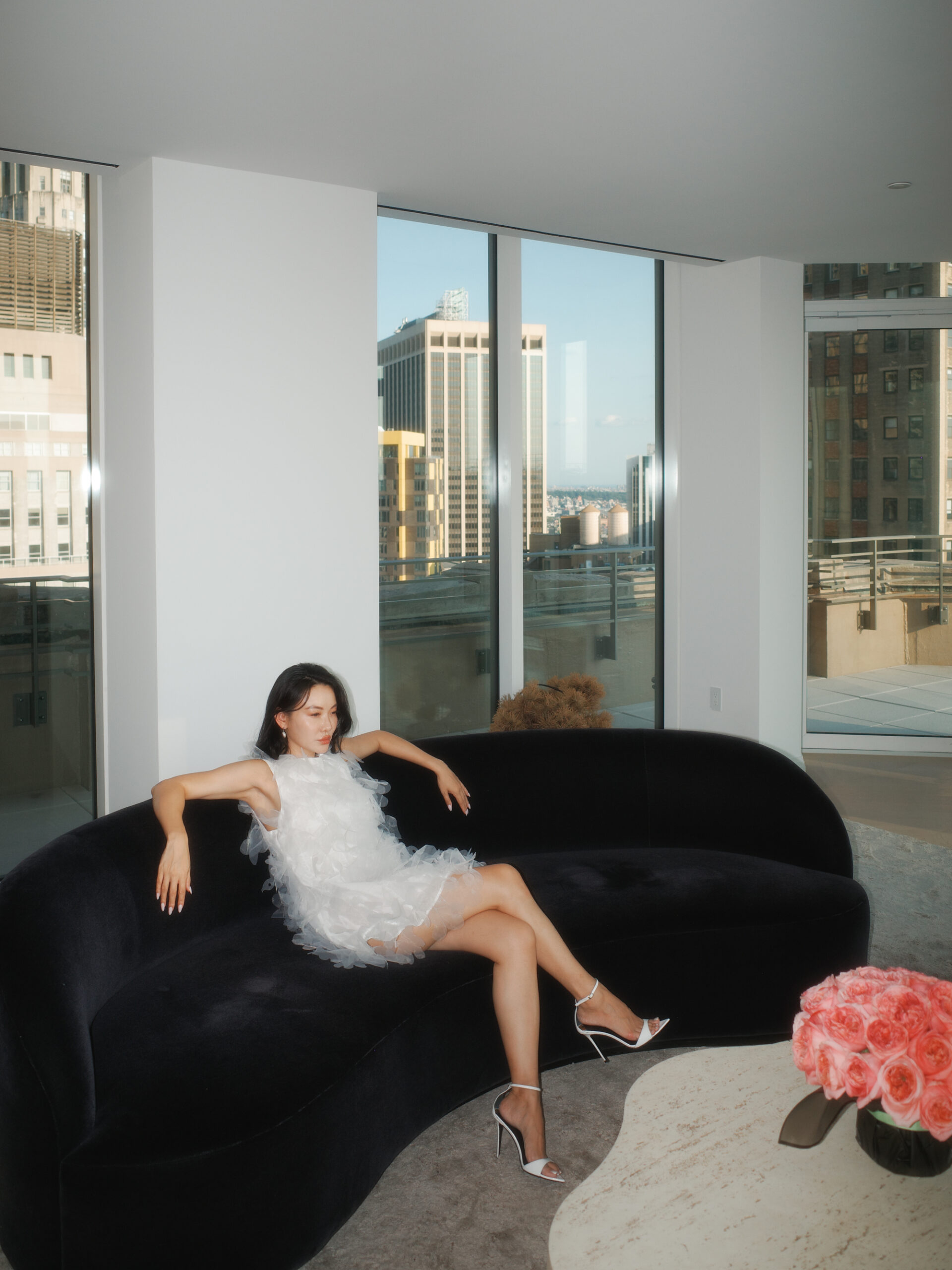 Jessica Wang reclining in a white textured mini dress and white stiletto sandals