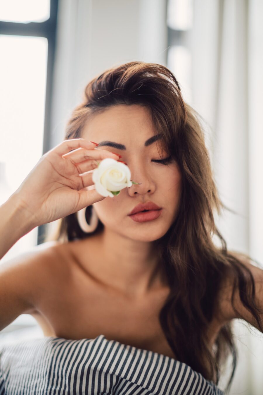 Jessica Wang holding a white rose beside her face in a close-up beauty portrait