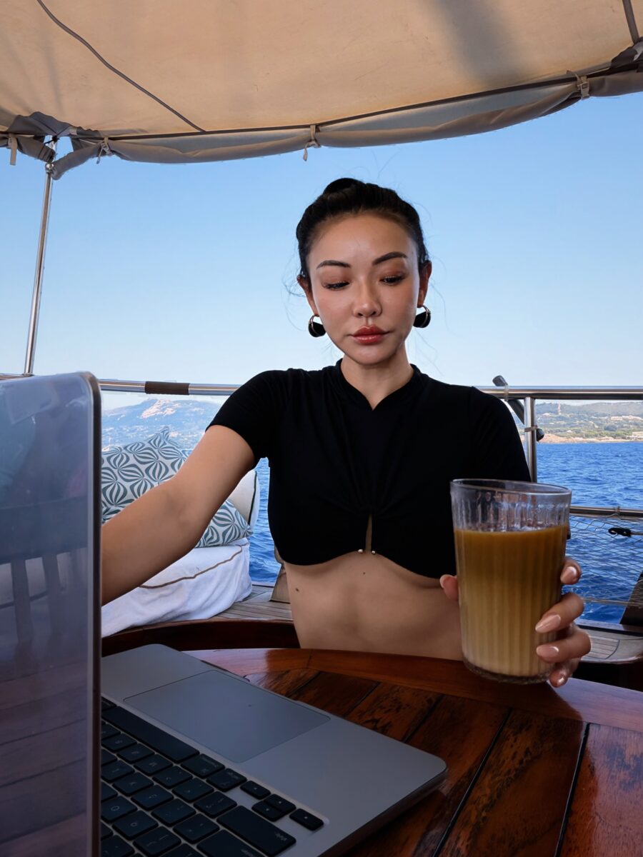 Jessica Wang working on a laptop at a table on a boat with the sea behind her