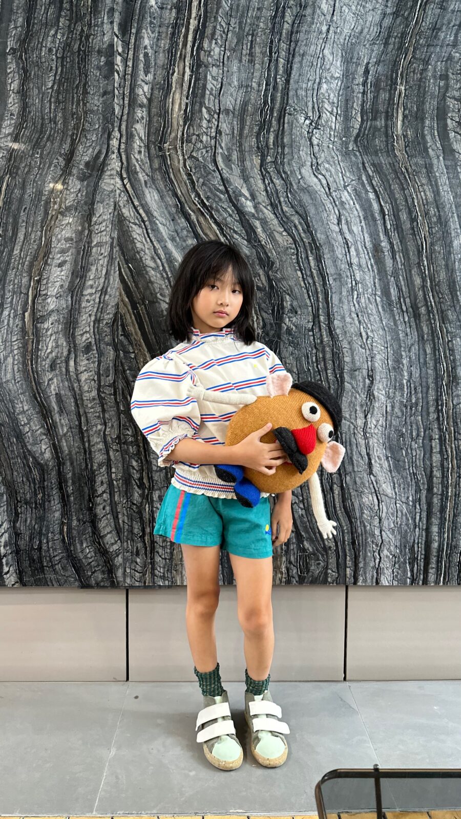 Child holding a Mr. Potato Head plush toy against a textured stone wall