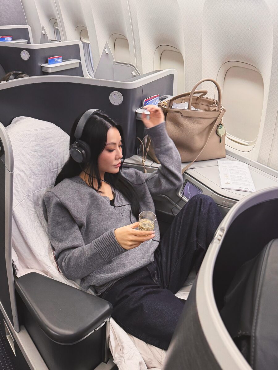 Jessica Wang wearing headphones in an airplane seat beside a taupe tote bag