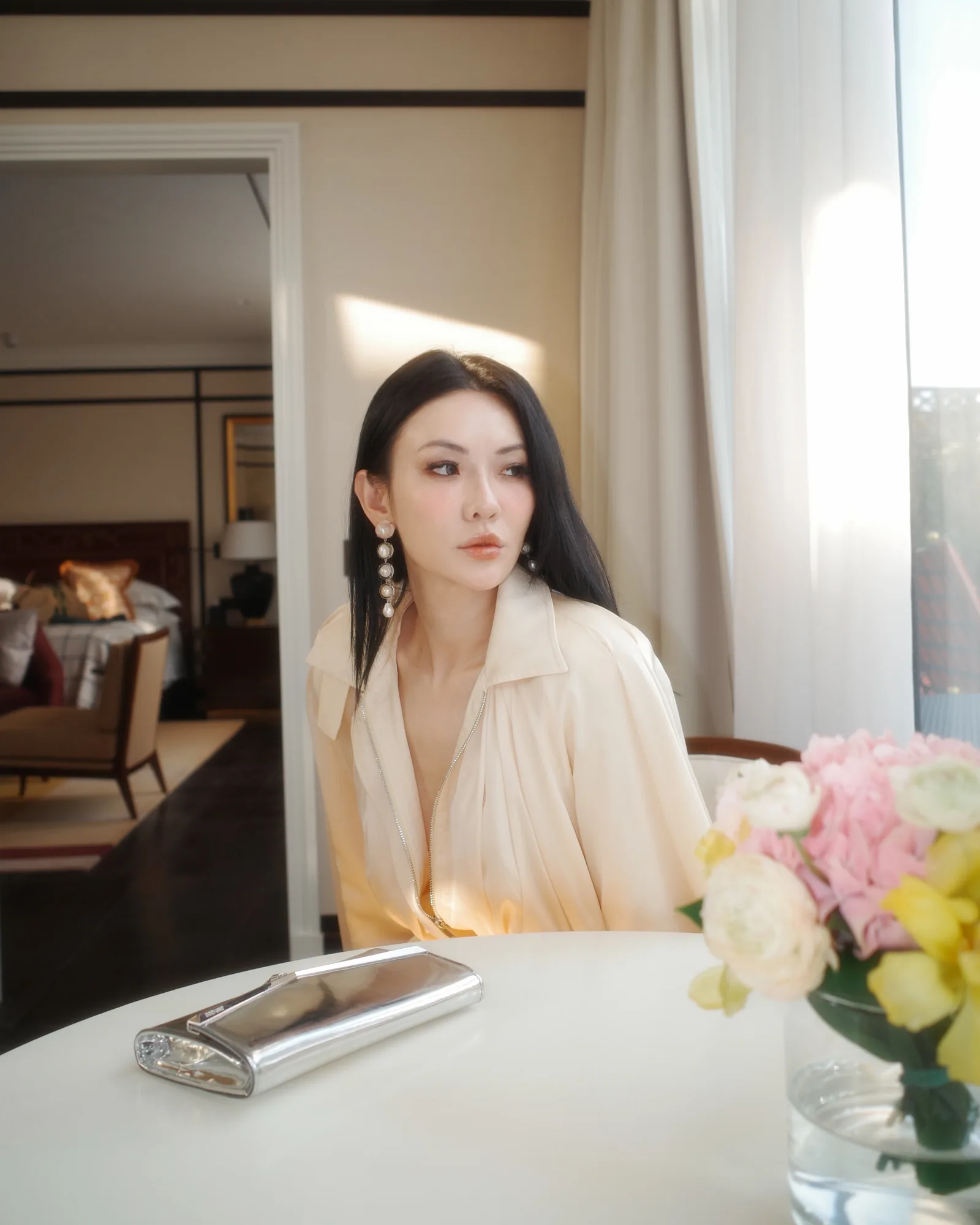 Jessica Wang in a cream blouse seated beside a window, with pink and yellow flowers in the foreground.