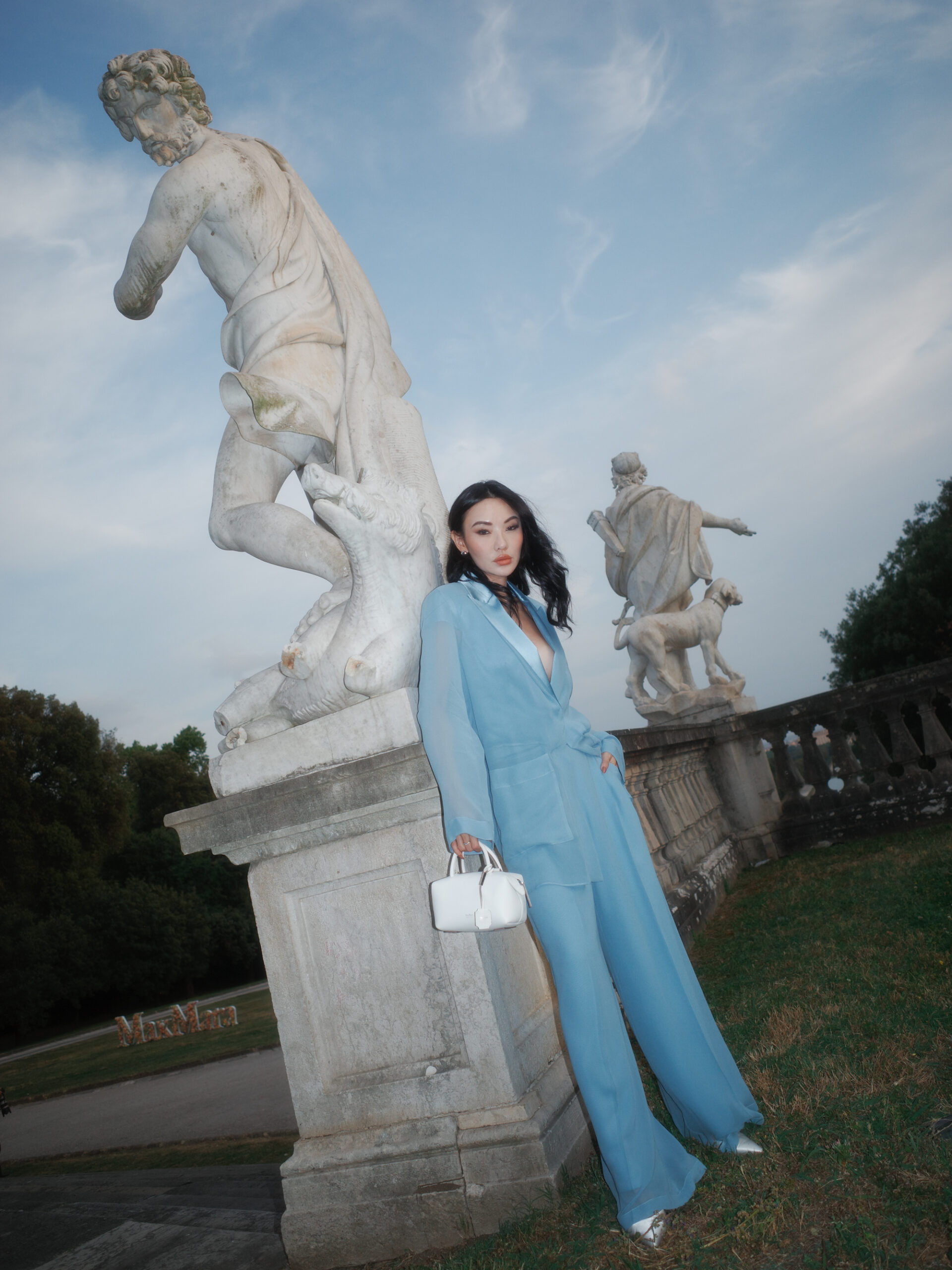 Jessica Wang wearing a light blue oversized pantsuit beside garden statues