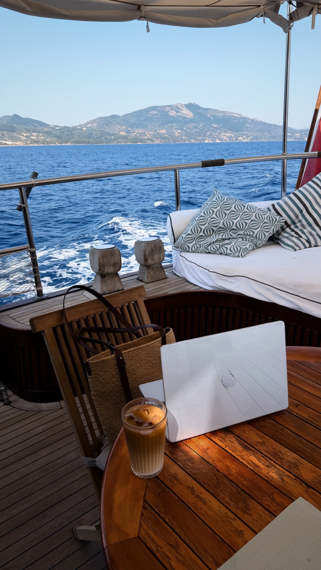 A laptop and drink arranged on a yacht table overlooking the sea